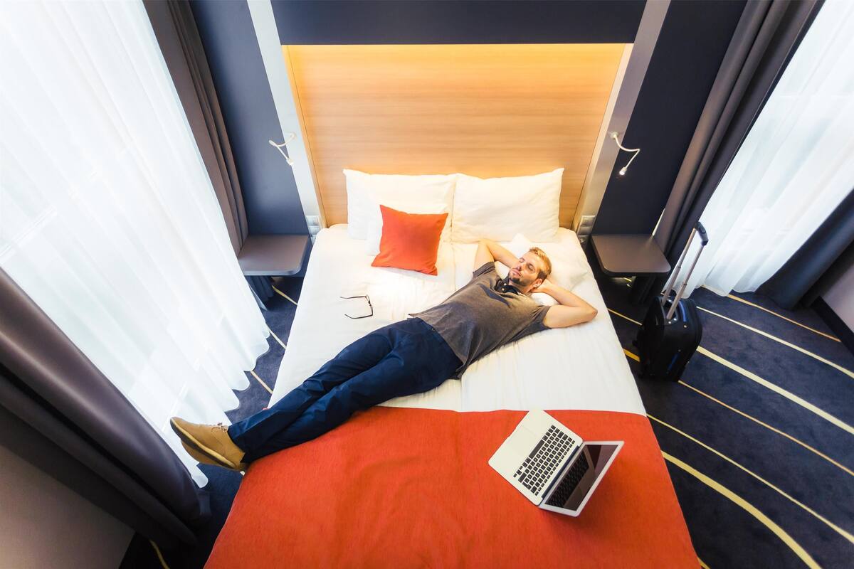 A hotel room with a bed, a laptop, and a suitcase.