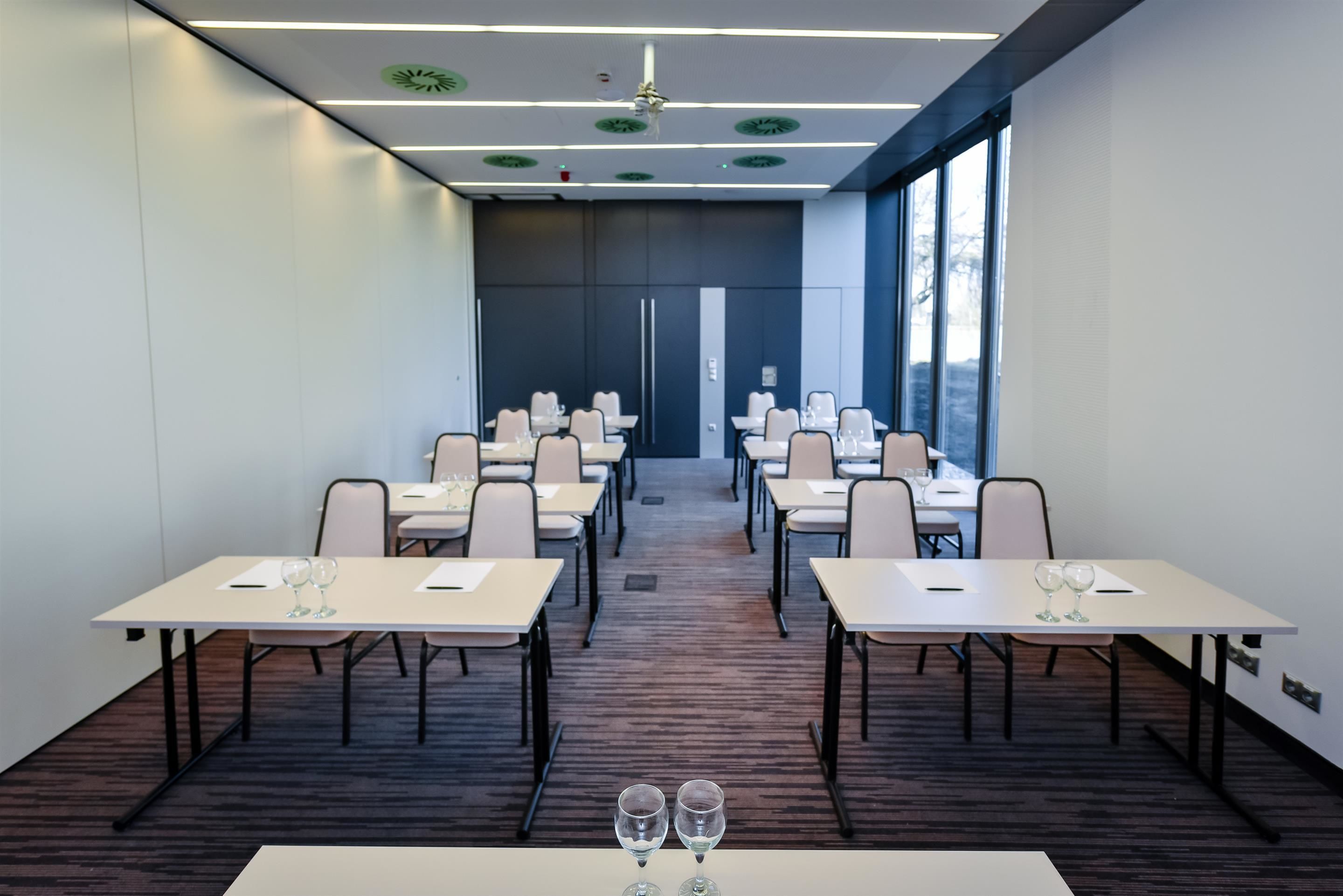 A conference room with multiple tables and chairs, equipped with water glasses.