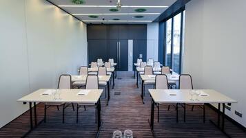 Un salón de conferencias con varias mesas y sillas, equipado con vasos de agua.