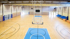 Una cancha de baloncesto con piso azul, un aro de baloncesto y sillas azules a lo largo de los lados.