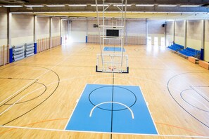 Una cancha de baloncesto con piso azul, un aro de baloncesto y sillas azules a lo largo de los lados.