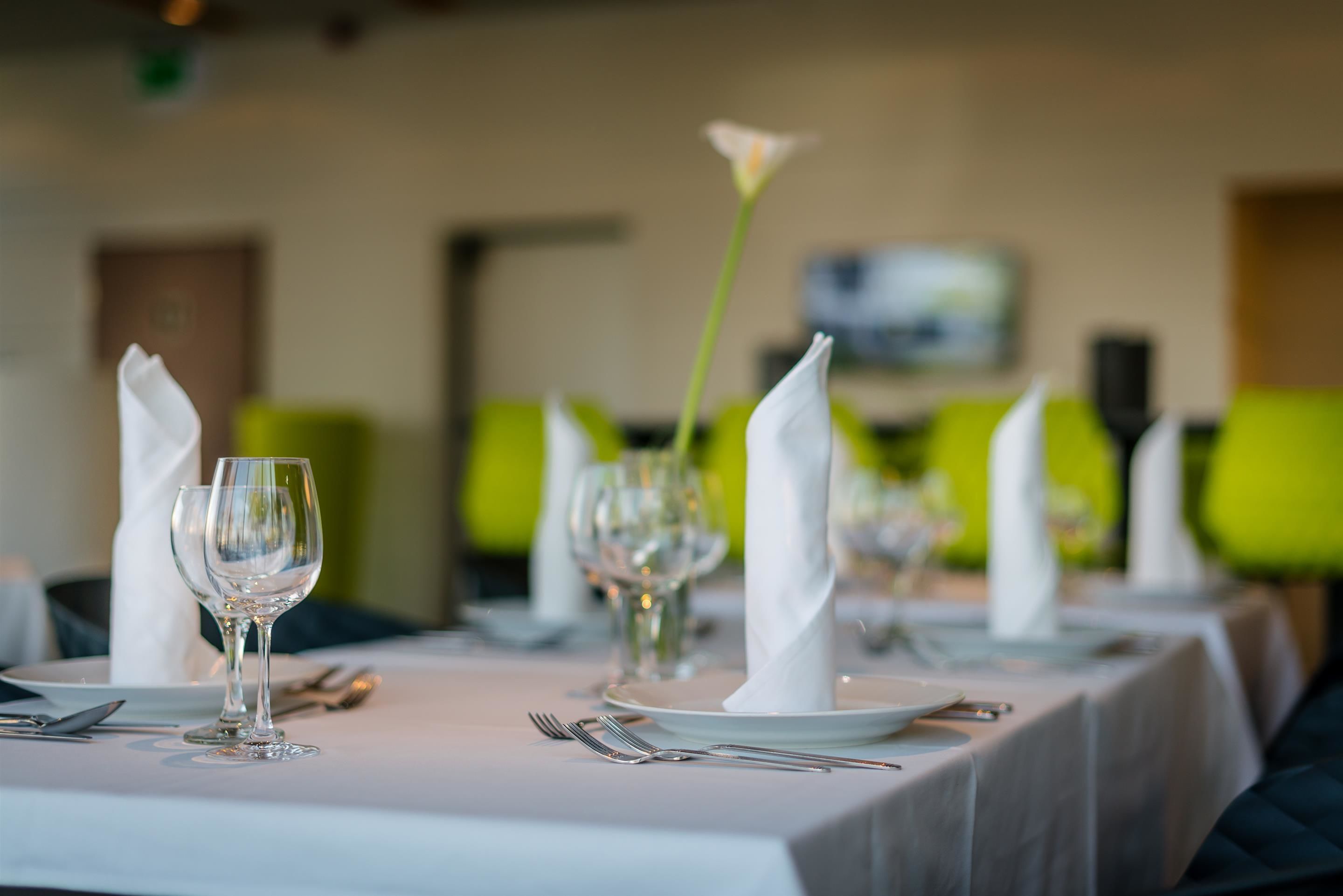 A dining table set with white napkins, wine glasses, and cutlery, with a green chair in the background.