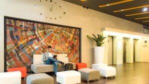 Un moderno vestíbulo de hotel con un cuadro abstracto grande, asientos cómodos, una planta en maceta y un reloj en la pared.