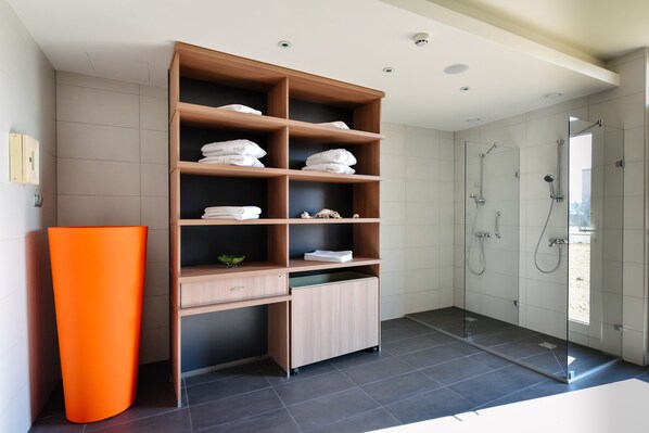 A modern bathroom with a wooden shelving unit, a glass shower enclosure, and a large orange vase.