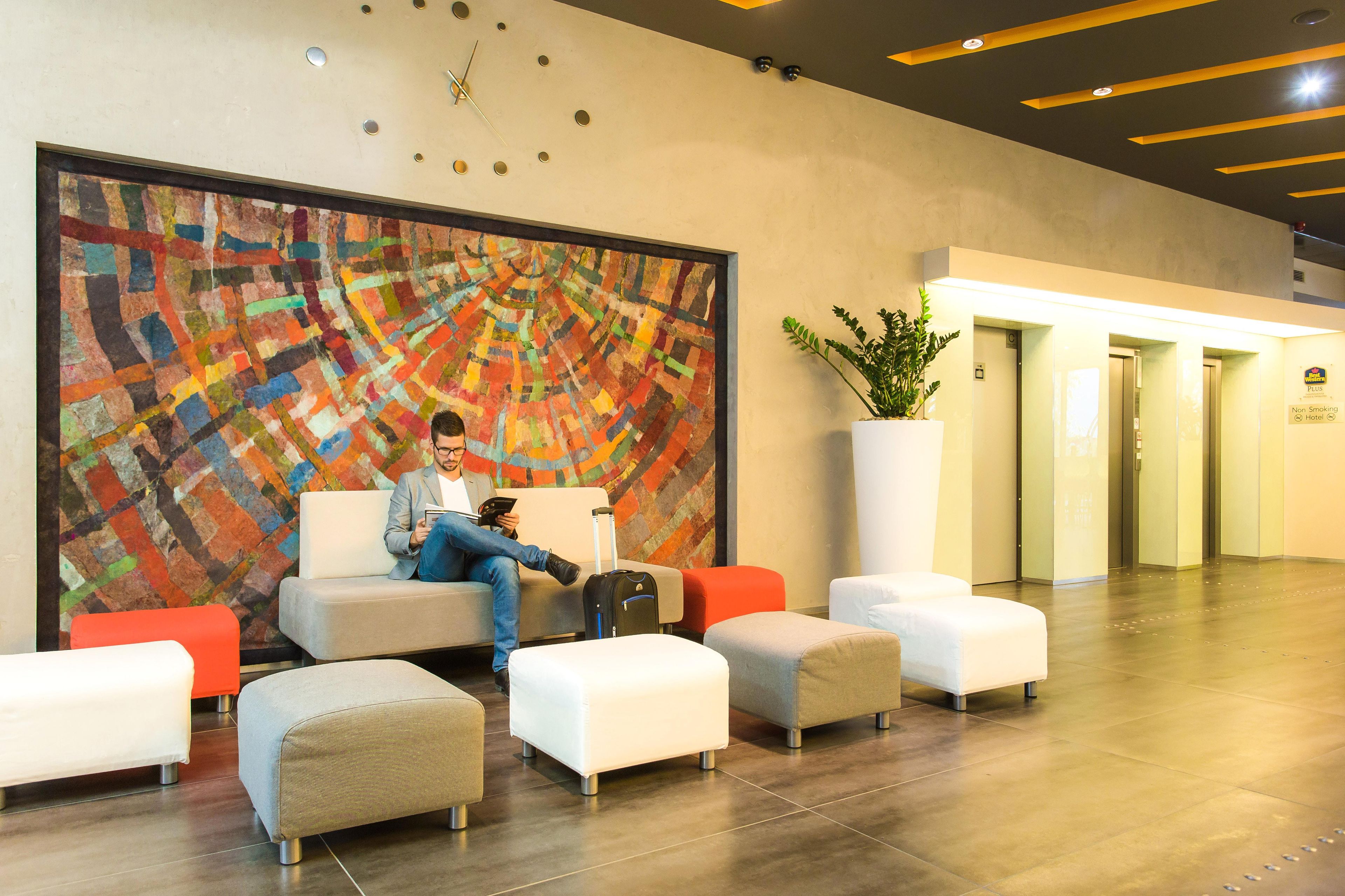 A hotel lobby with a large abstract painting, seating area, and a potted plant.