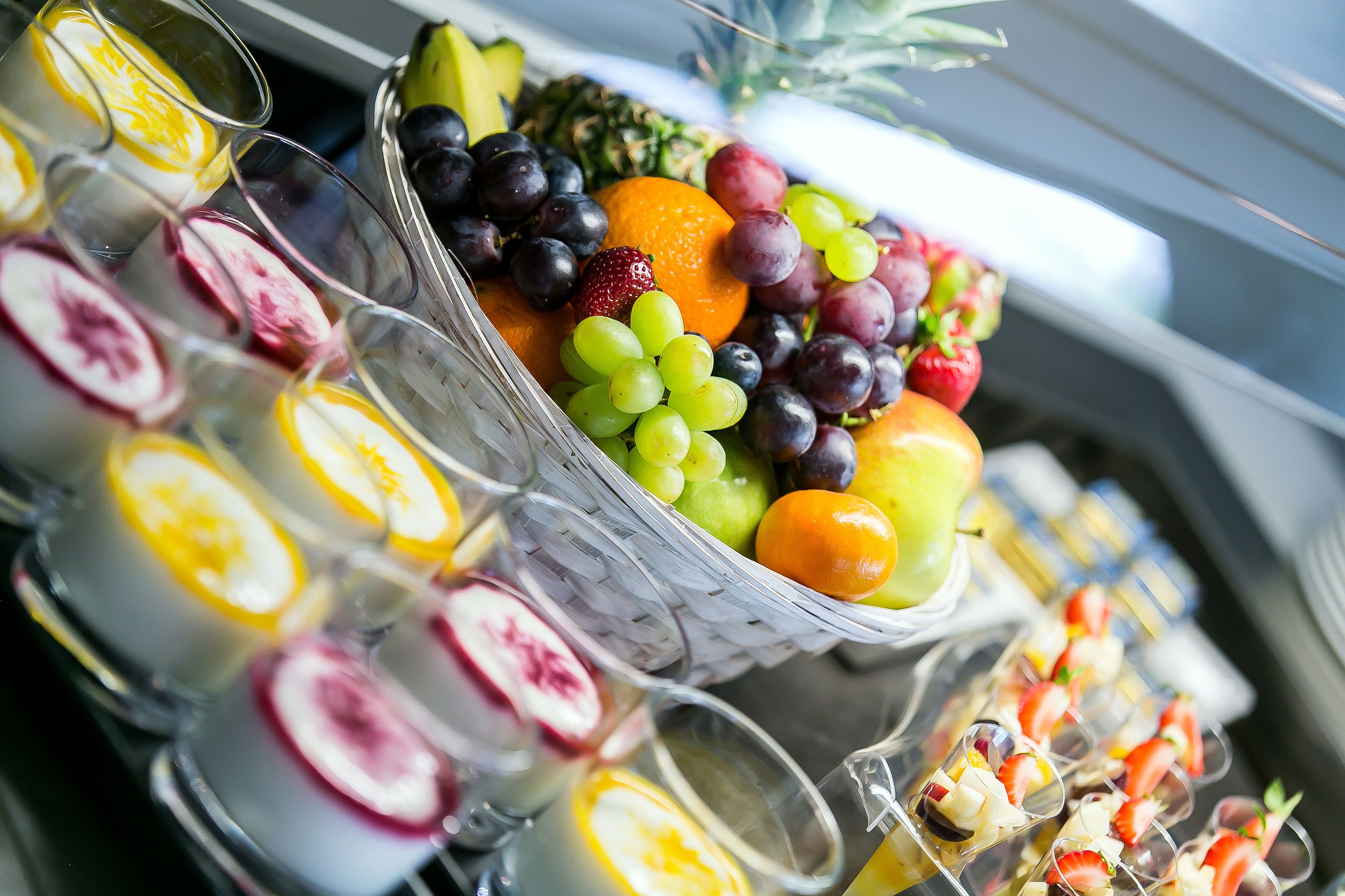 A fruit and dessert buffet with various fruits, including grapes, strawberries, and oranges, and several glasses of beverages.
