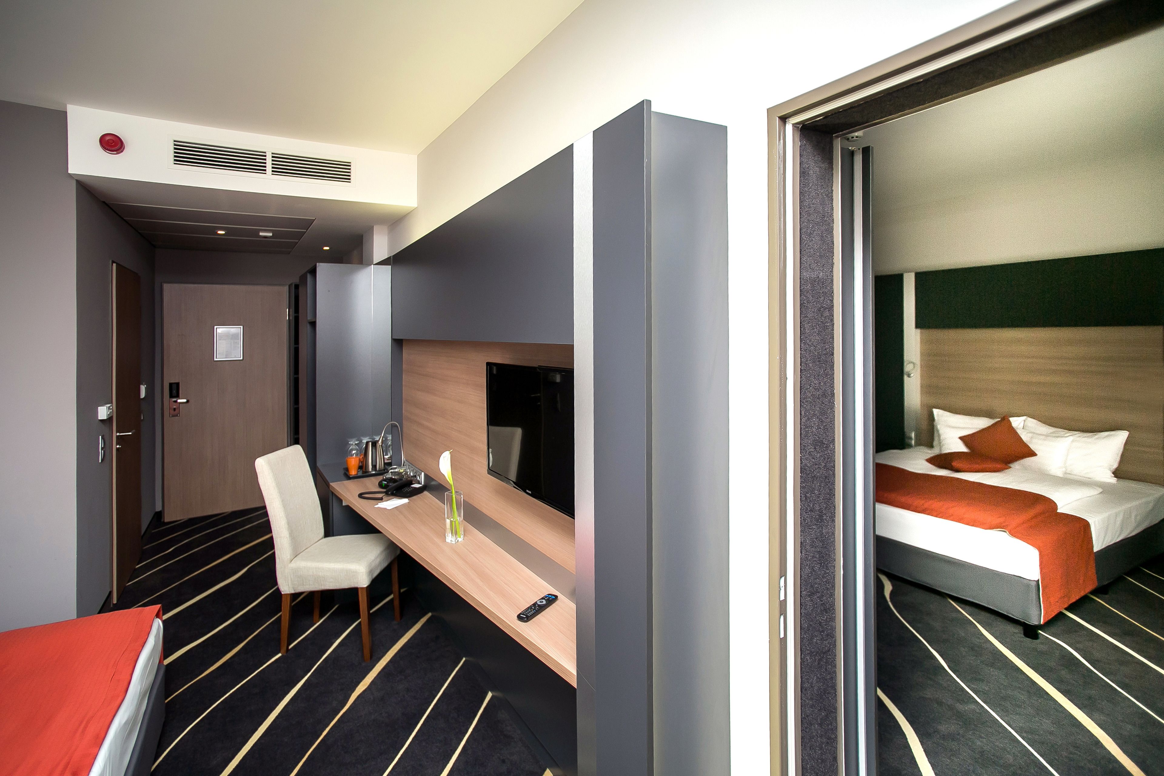 Ein Hotelzimmer mit einem Bett, einem Schreibtisch mit Stuhl, einem Fernseher und einem kleinen Tisch mit Glas und Flasche.