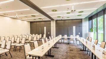 Un salón de conferencias con mesas largas, sillas y una pantalla de proyector.
