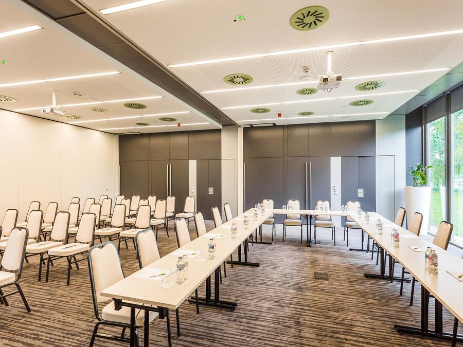 Un salón de conferencias con mesas largas, sillas y una pantalla de proyector.