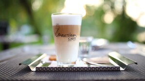 Una taza de Caffè con una etiqueta, sobre una mesa con un fondo verde desenfocado.