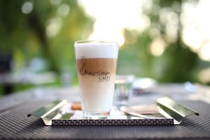 Una taza de Caffè con una etiqueta, sobre una mesa con un fondo verde desenfocado.