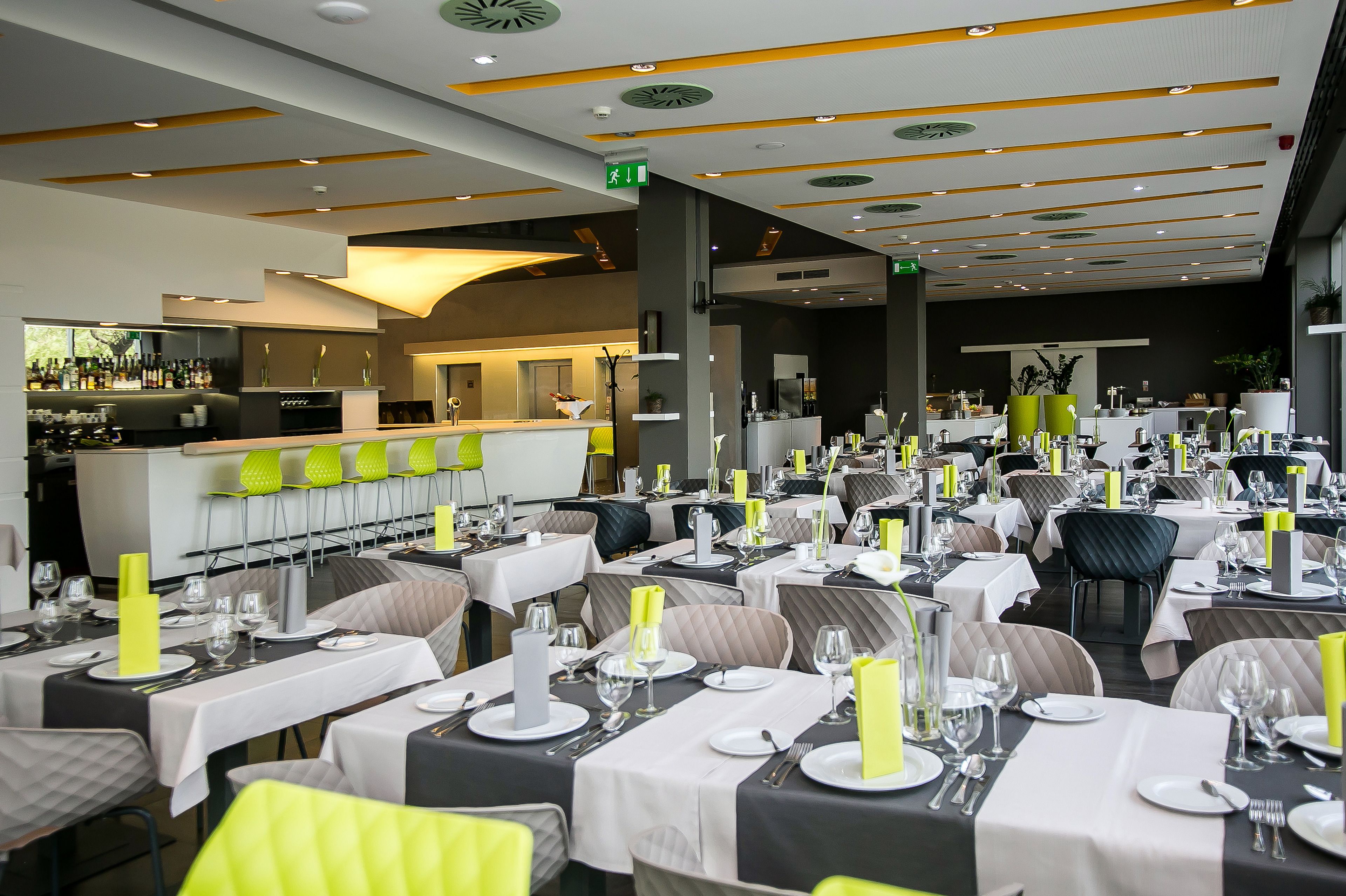 Un restaurant doté de nombreuses tables dressées pour le service, d’un espace bar et d’un design de plafond moderne.