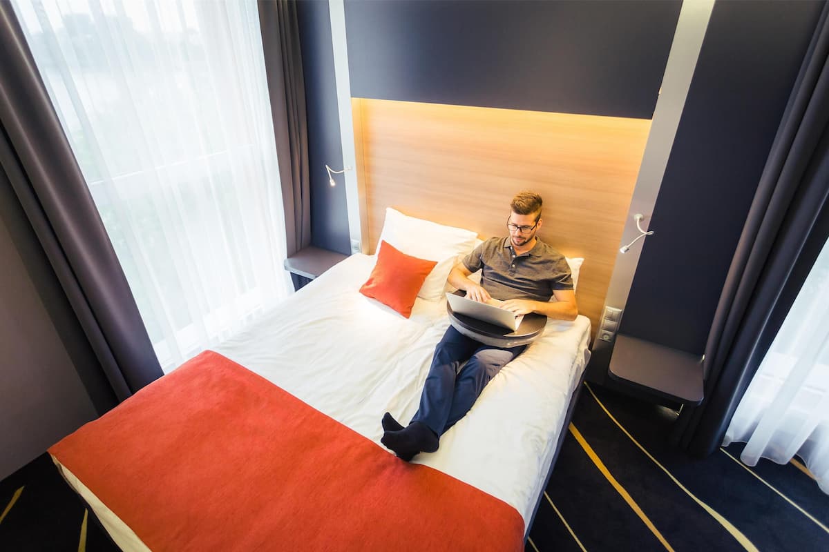 A hotel room with a bed, a laptop, and a window with curtains.