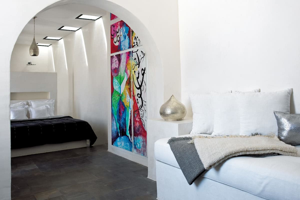 A modern bedroom with a bed, a large abstract painting, and a unique ceiling design.