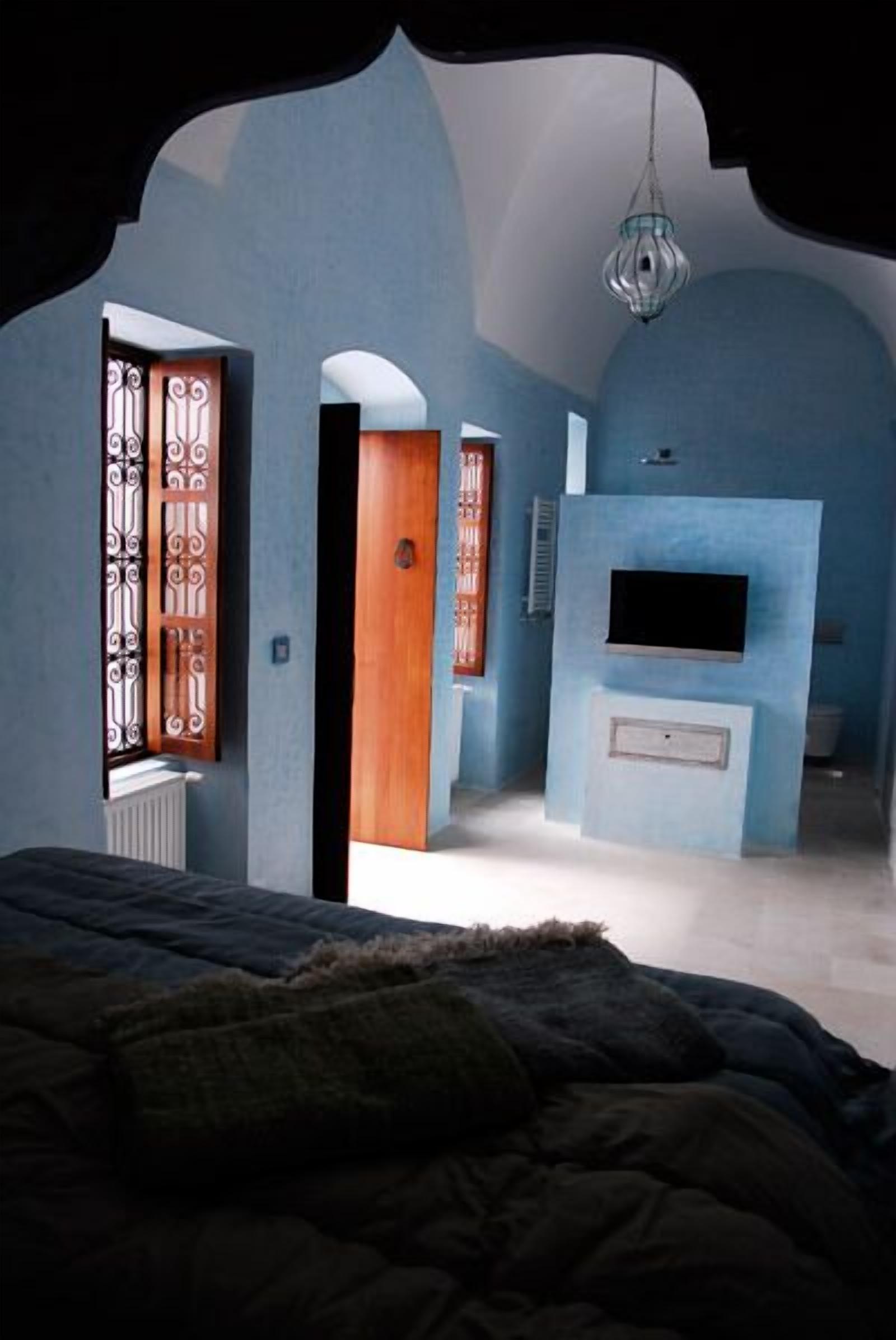 A bedroom with a bed, a TV mounted on the wall, and a window with decorative metal bars.