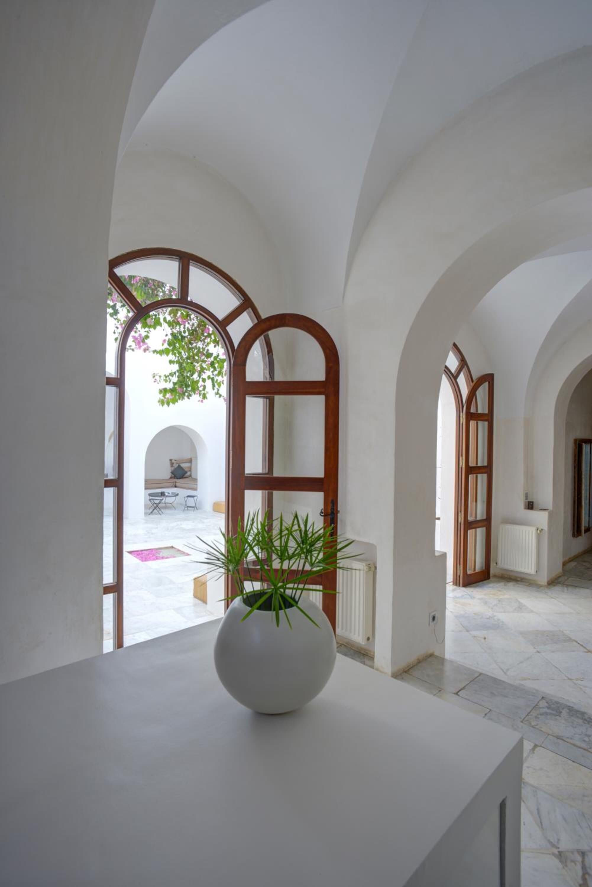 Un couloir avec des portes en arc donnant sur une pièce où se trouvent une table blanche et une plante en pot.