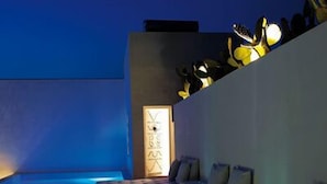 Un espace extérieur moderne aménagé avec un canapé et une petite table, une horloge murale et une composition décorative de cactus.