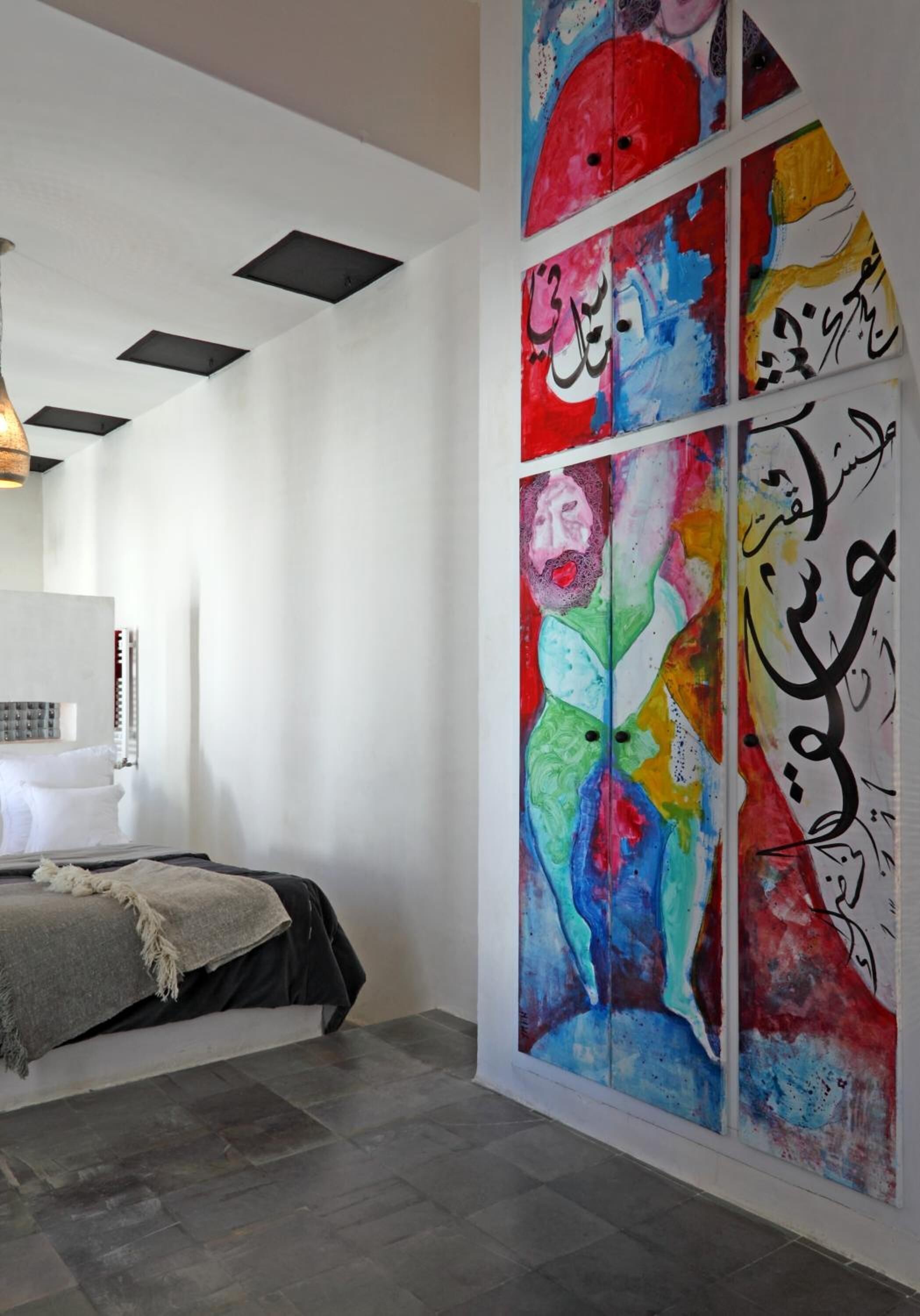 Un dormitorio moderno con un cuadro abstracto grande en la pared, una cama con manta gris y un techo con iluminación empotrada.
