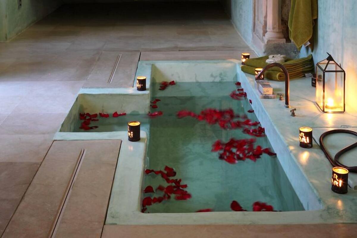 A bedroom with a large ornate bed, a bathtub with rose petals, and candles.