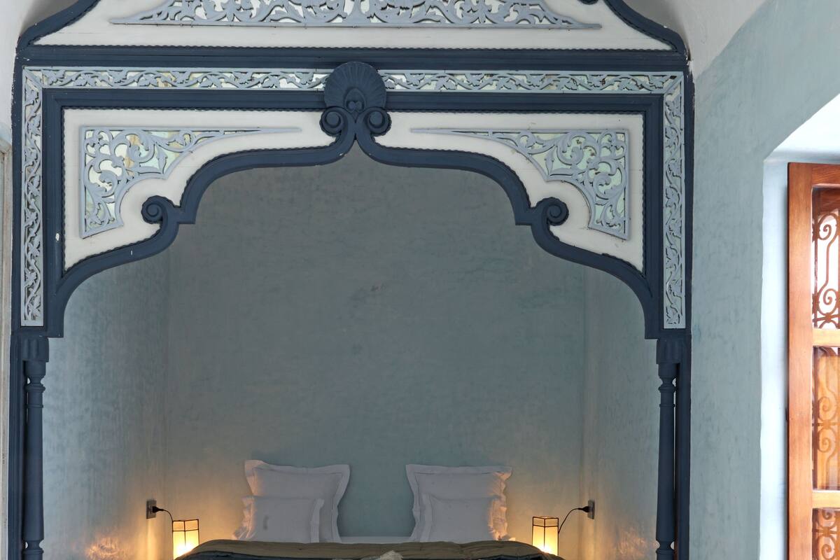 A bedroom with a four-poster bed, two bedside lamps, and a decorative ceiling.