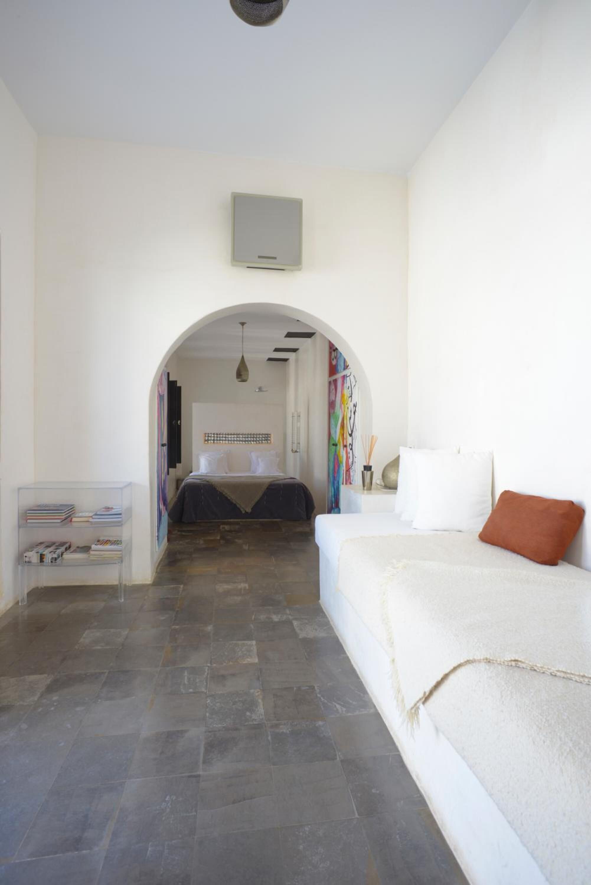 A bedroom with a bed, a reading area with books, and a hallway leading to another room.