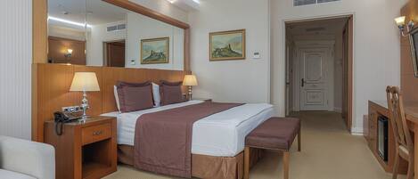 Une chambre d’hôtel avec un grand lit, des tables de chevet, un bureau, une chaise, un miroir et une porte donnant sur une autre pièce.
