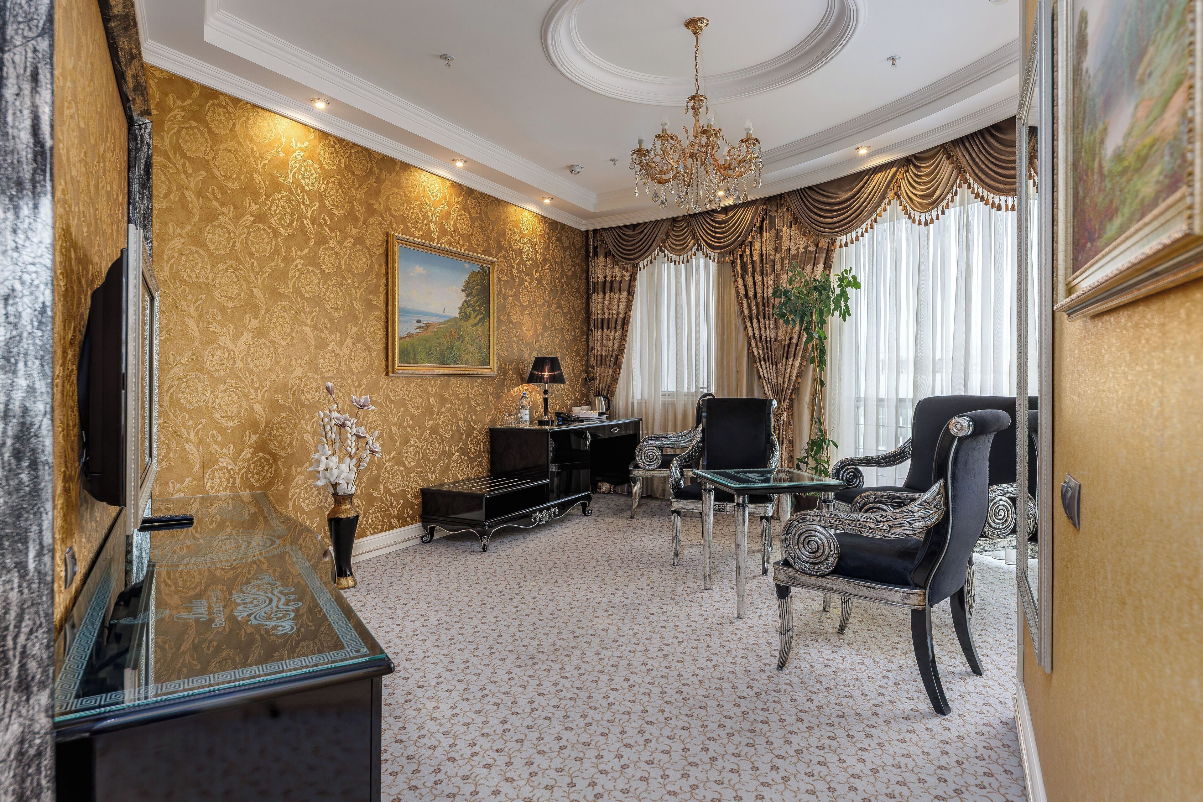A luxurious room with a patterned carpet, a chandelier, a television, a sofa, and a dining table.