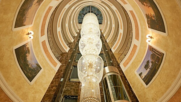 A grand, multi-level atrium with a central chandelier, marble floors, and framed artwork on the walls. - Boutique Hotel Buta (Minsk)