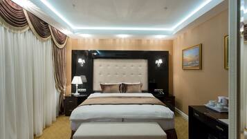 Hotelkamer met een groot bed, hoofdeinde, nachtkastjes, een bankje, gordijnen, een schilderij en een bureau met lamp.