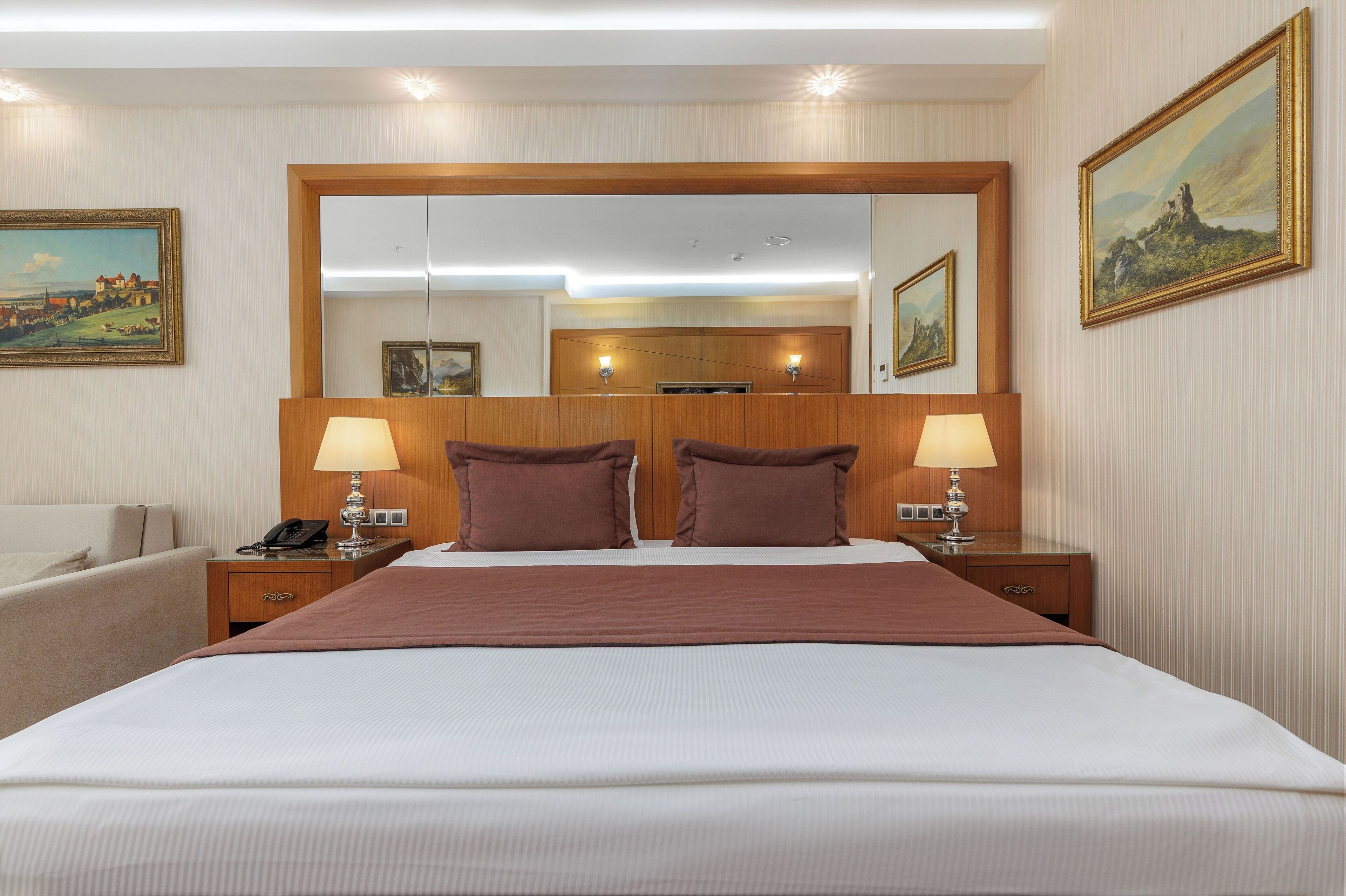 Een hotelkamer met een groot bed, twee nachtkastjes met lampen, een houten hoofdeinde en twee ingelijste foto's aan de muur.