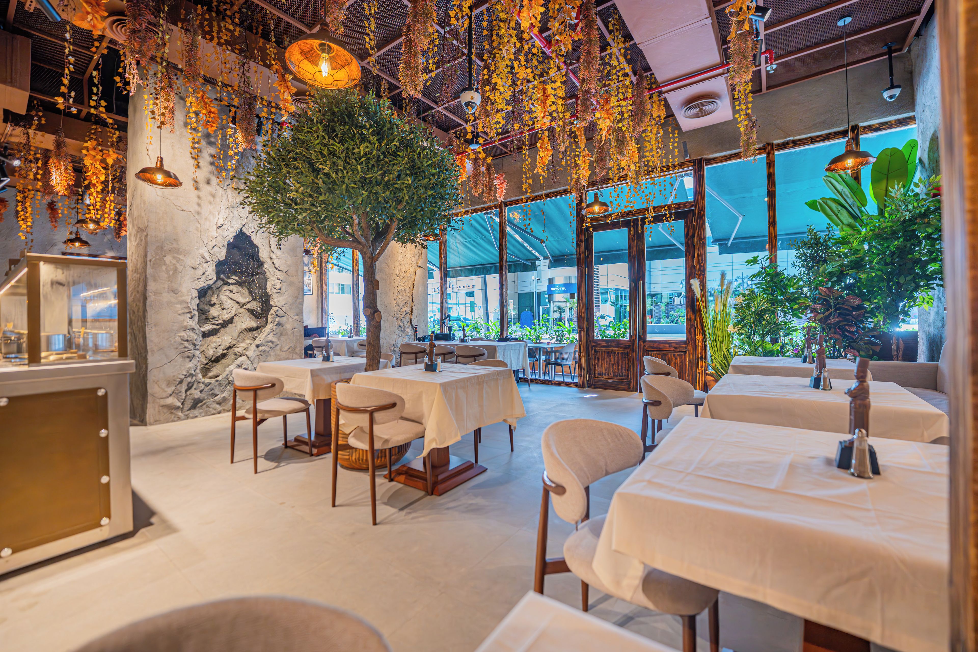 Een restaurant met tafels en stoelen, een grote boom en hangende planten.