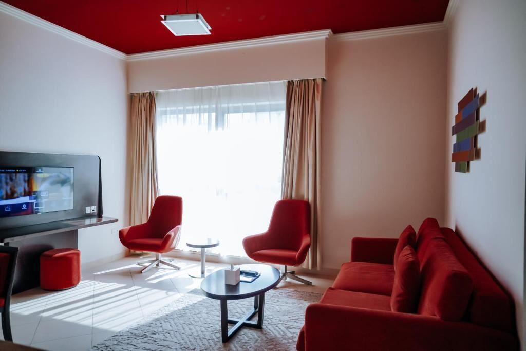 A modern living room with a red sofa, two red armchairs, a coffee table, and a flat-screen TV on a stand.