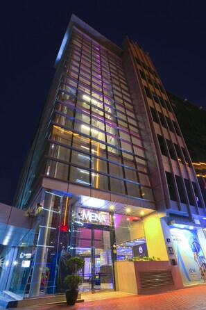 A modern hotel with a glass facade, illuminated signage, and a prominent entrance. - Mena Aparthotel (Dubai)