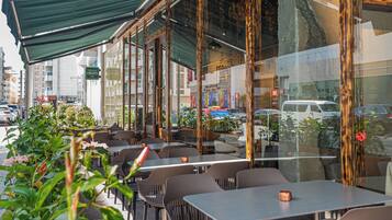 Un cafè a l'aire lliure amb taules i cadires, una zona coberta i vista al carrer.