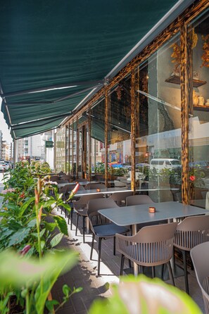 Un café al aire libre con mesas y sillas, un área cubierta y vistas a la calle.
