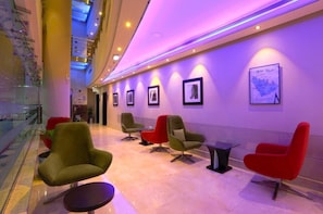 A modern lobby with a glass railing, a seating area with green and red chairs, and framed artwork on the walls. - Mena Aparthotel (Dubai)