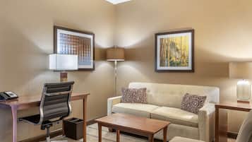 A hotel room with a desk, office chair, sofa, and a small table.