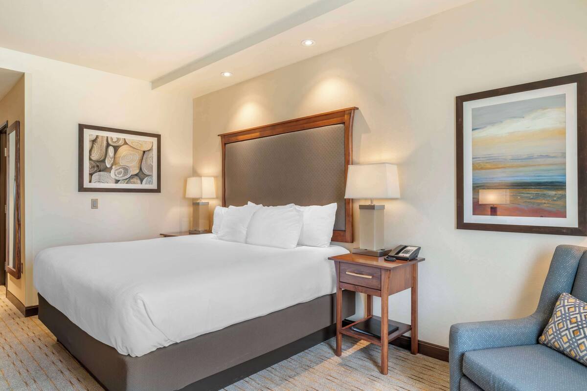 A hotel room with a large bed, bedside lamps, a nightstand, a chair, and artwork on the walls.