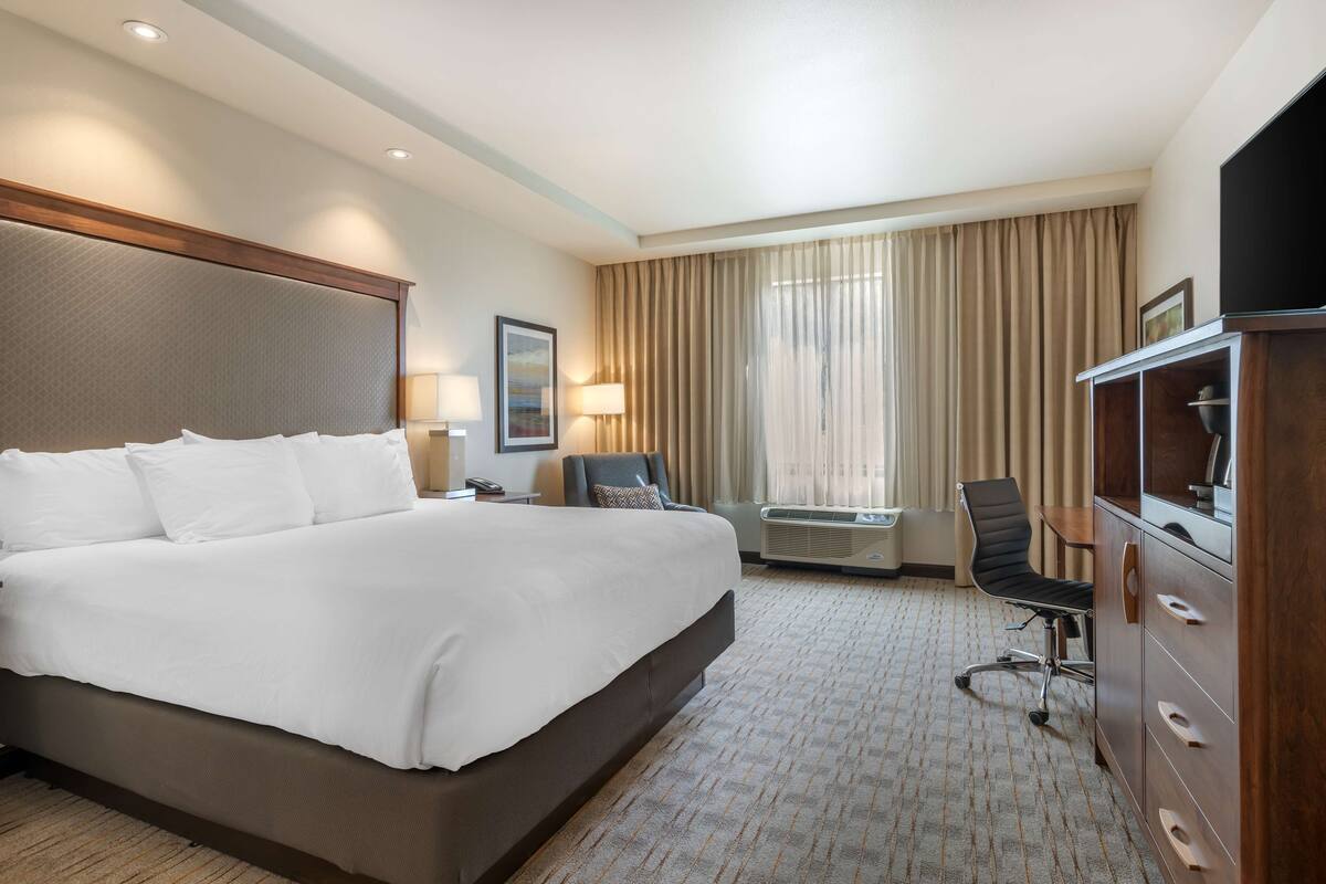 A hotel room with a large bed, a desk with a chair, a television, and a minibar.