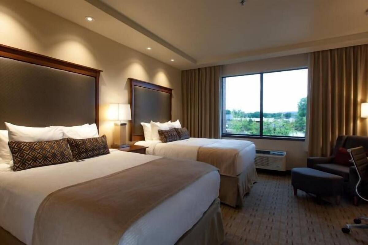A hotel room with two beds, a desk, and a chair.