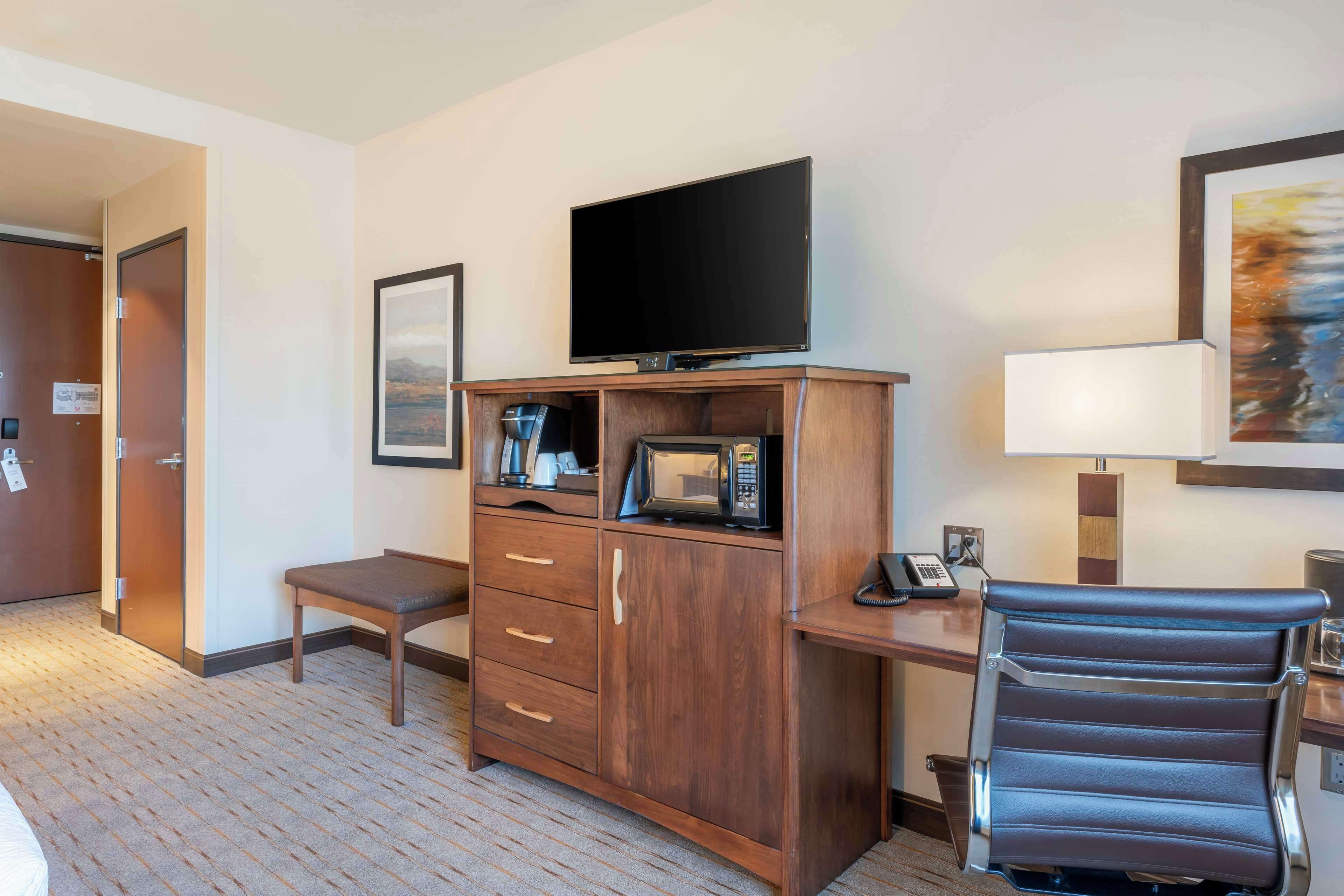 A hotel room with a wooden cabinet, a flat-screen TV, a microwave, a desk, a chair, and a framed picture on the wall.