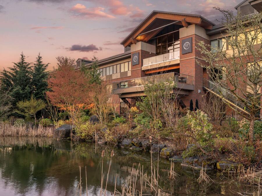 A modern building with a reflective pond, surrounded by autumn foliage and a clear sky.