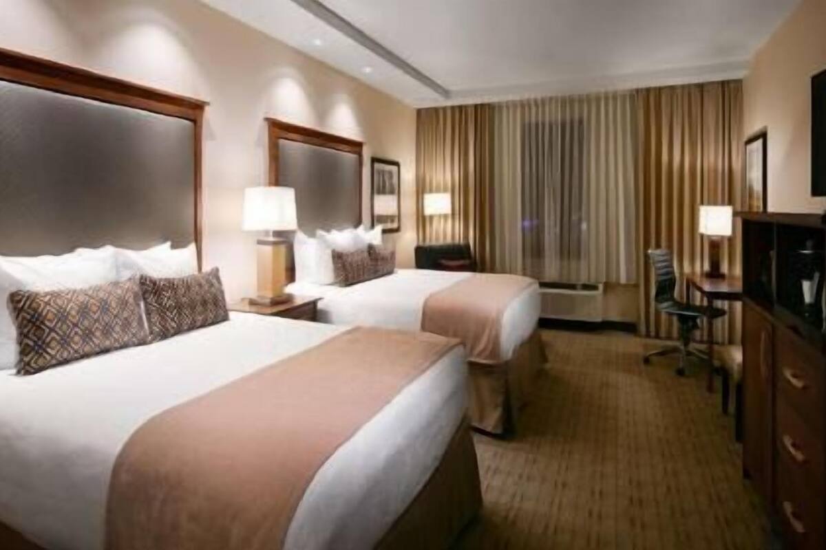 A hotel room with two beds, a desk, a chair, a TV, and a window with curtains.