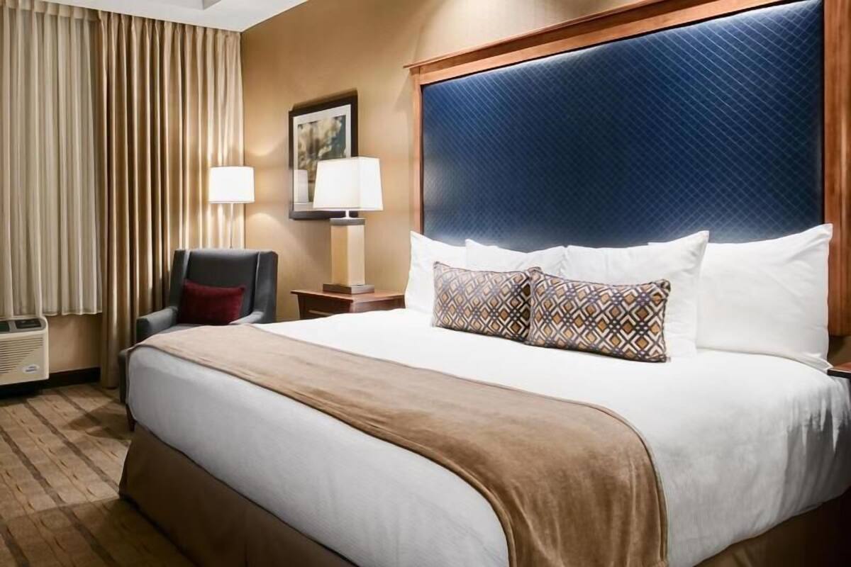 A hotel room with a large bed, a desk, two lamps, a chair, a picture on the wall, and a window with curtains.