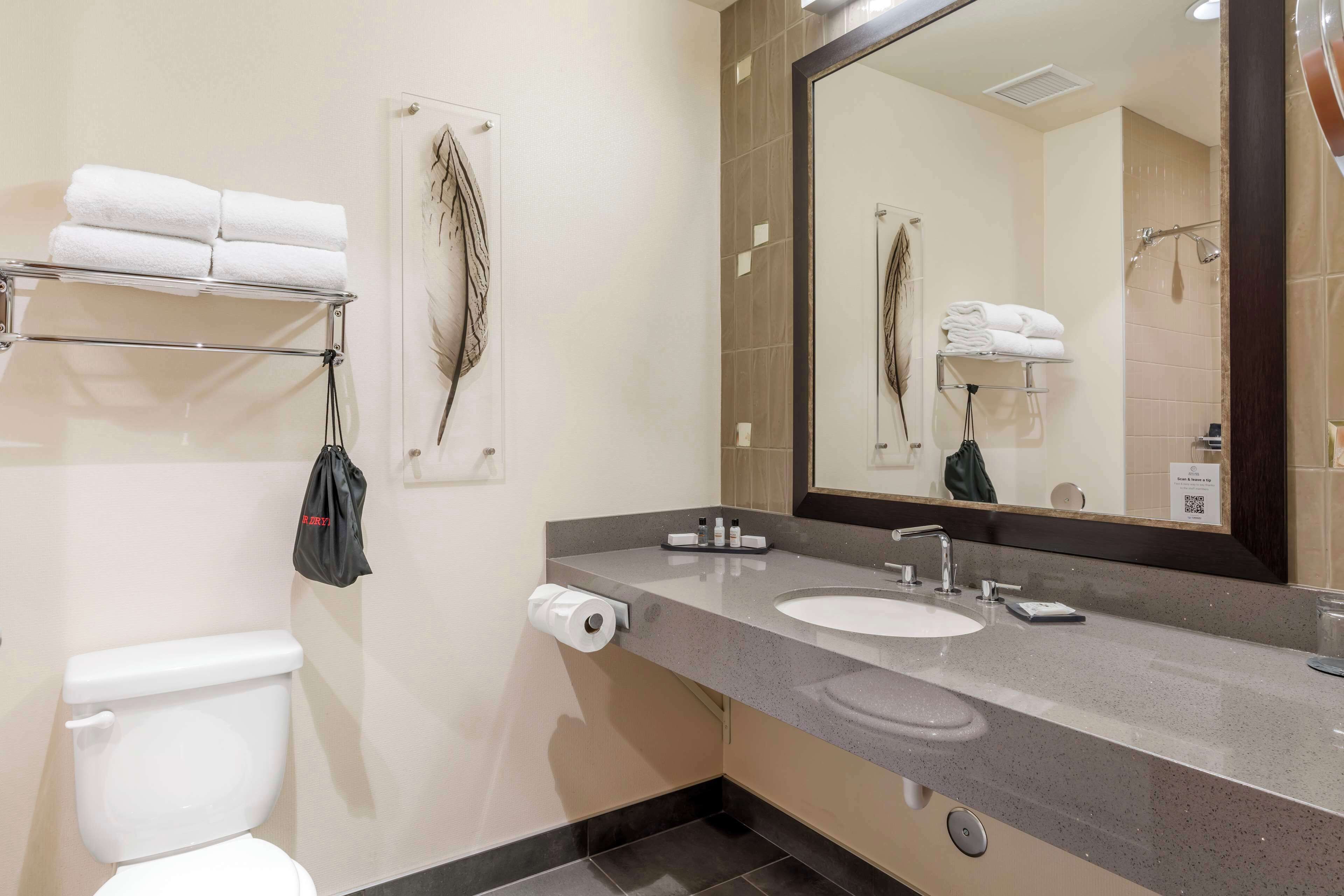 Un baño moderno con inodoro blanco, lavamanos con un espejo grande y toallero con toallas dobladas.