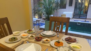 A dining table set with plates, bowls, and cutlery, overlooking a pool area.