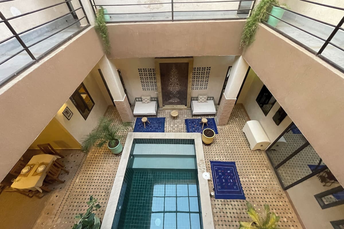 Um pátio com piscina central, áreas de estar e plantas em vasos.