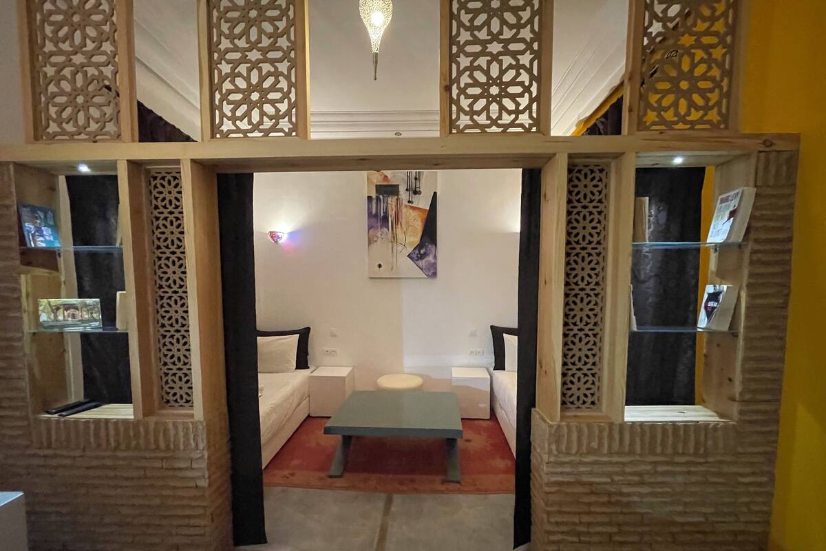 Uma sala de estar com sofá, mesa de centro e painéis decorativos. Prateleiras com objetos nas paredes.
