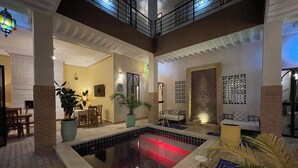A spacious indoor area with a central pool, seating areas, and a staircase leading to an upper level.
