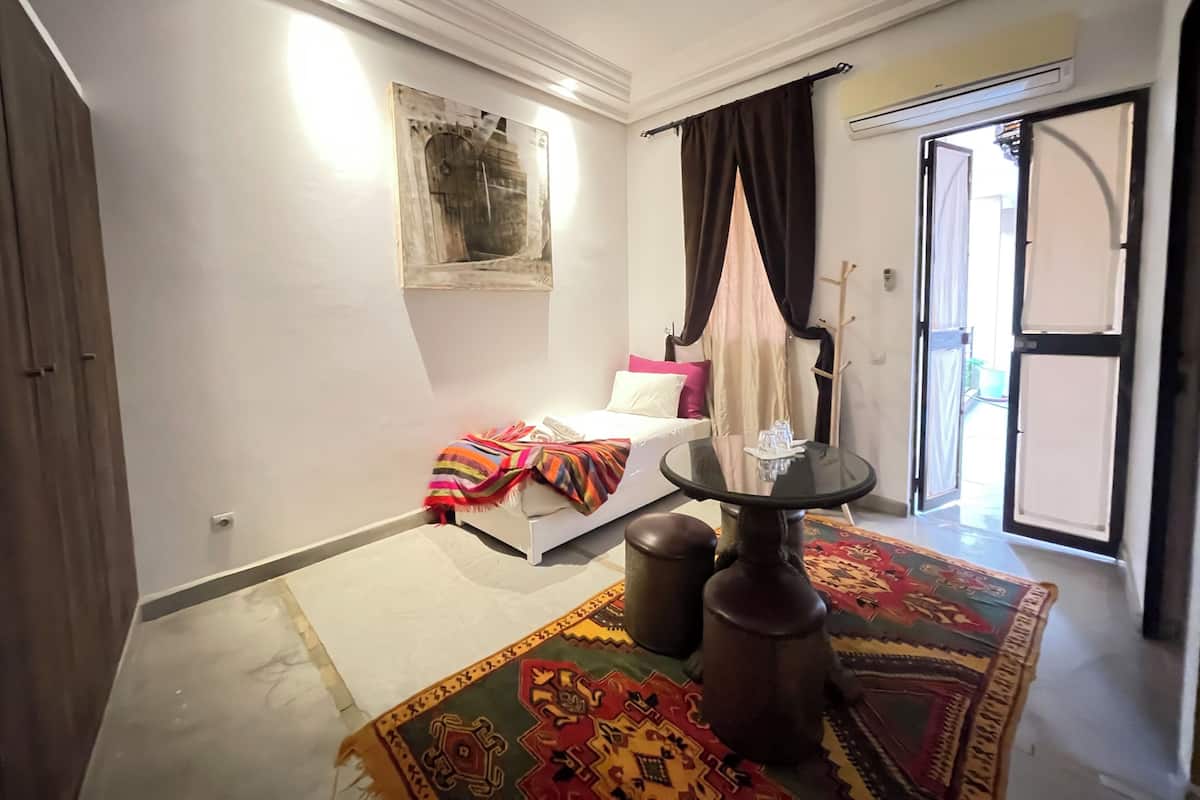 Quarto com cama, uma mesinha com copos, um porta-roupas e um tapete colorido.